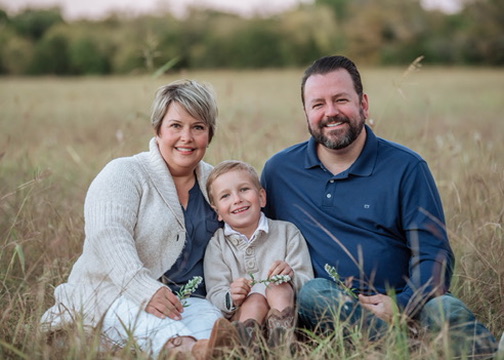 Ryan seated in a field with his wife and son
