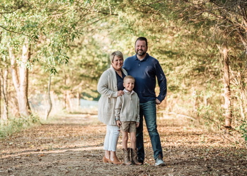 Ryan standing on a wooded path with his wife and son